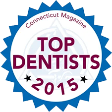 The image displays a badge with text that reads  CONNECTICUT MAGAZINE TOP DENTISTS 2015  and features a graphic of a shield and a stylized depiction of a dentist s chair. It also includes the logo for Connecticut Magazine at the top right corner. The style of the badge suggests it is an award or recognition given to dental professionals in the state of Connecticut.