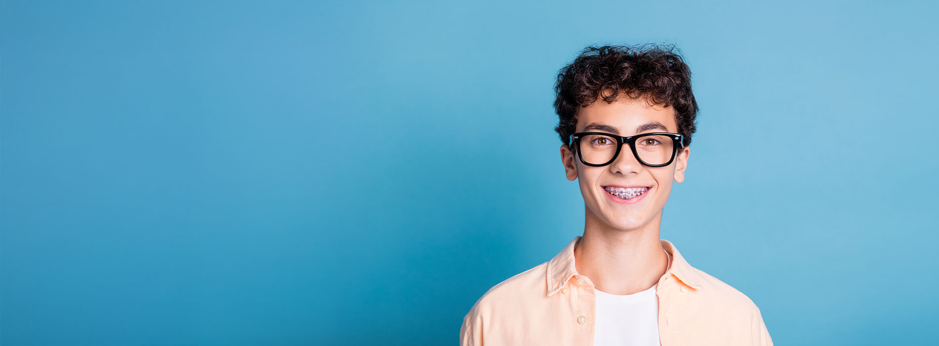 The image shows a person standing against a blue background with a smiling expression, wearing glasses and a light-colored top, appearing to be in front of a digital overlay that obscures part of their body.