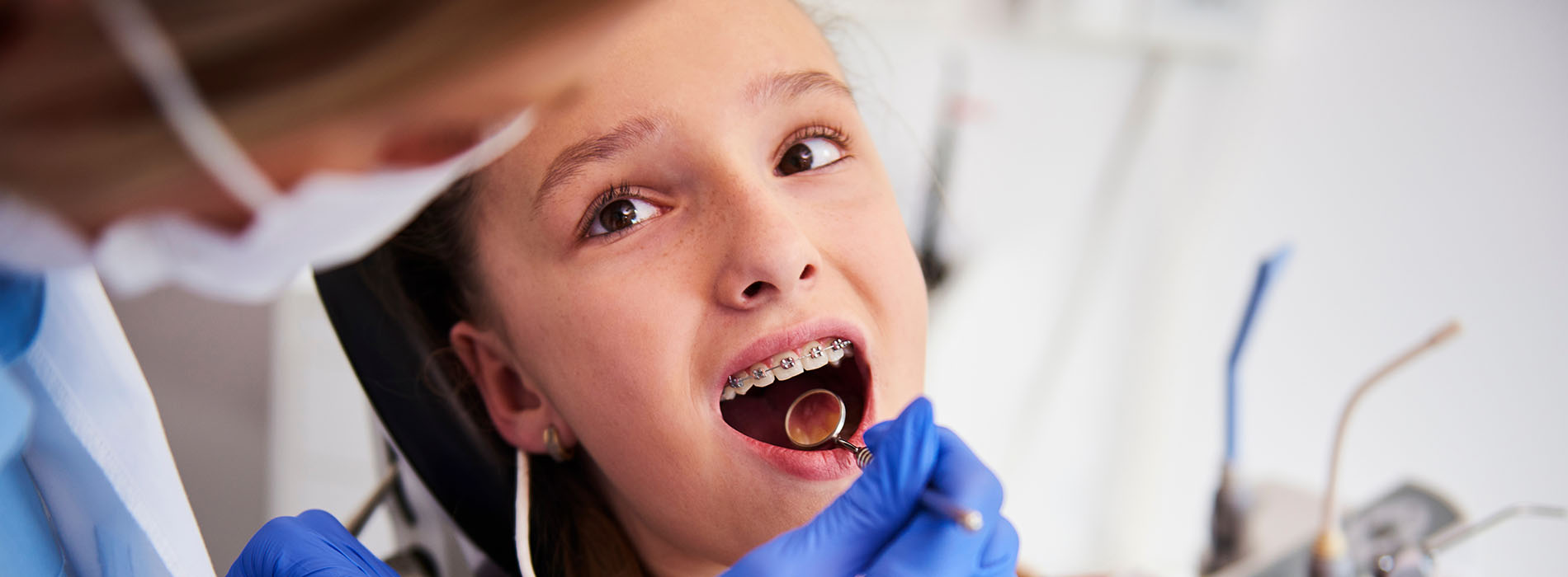 A young girl with braces smiling at the camera while seated in a dental chair.