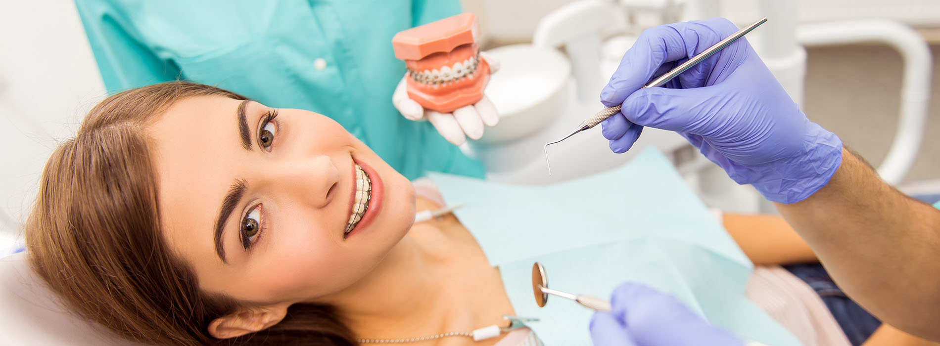 A woman sitting in a dental chair receiving dental treatment with a dentist at work behind her.