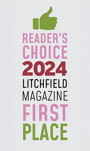 The image features a graphic design with text overlaying a photograph. At the top, there s a stylized green checkmark with the word  READER S CHOICE  beneath it in bold, uppercase letters. Below this, a large number  2021  is prominently displayed, followed by the name  LITCHFIELD MAGAZINE  in smaller uppercase letters. A pink stripe separates the text from the photograph below. The photo shows a magazine cover with the headline  FIRST PLACE  and the subheadline  READER S CHOICE 2021.  The cover features a graphic element resembling a trophy or award, and there is a small pink ribbon with the text  LITCHFIELD MAGAZINE  on it. The overall style of the image suggests an advertisement or promotional material for a magazine that has won some sort of recognition in 2021. The design uses a clean, modern aesthetic with a color scheme that includes shades of green and pink.