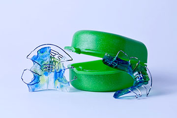 The image shows a pair of green scissors with a clear plastic handle, placed against a white background.