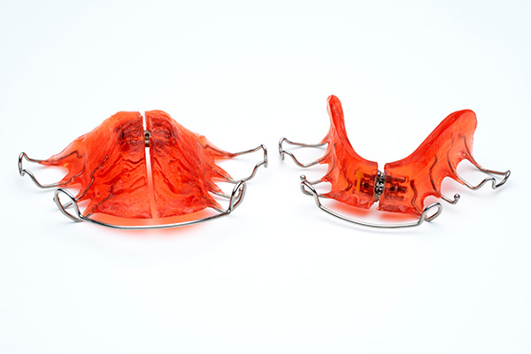 The image shows two red dental mouthguards with a playful design resembling fish fins, placed side by side against a white background.