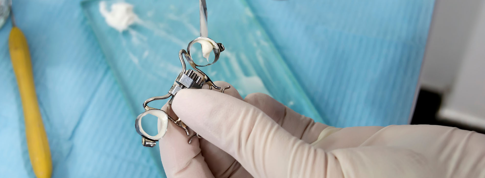 A pair of hands holding a small metal tool over a blue cloth background.