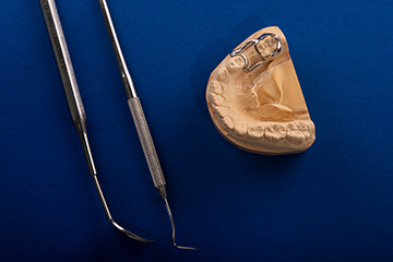 The image shows dental instruments on a blue background, with a focus on a tooth model and a dental drill.