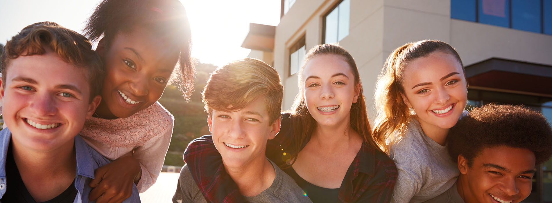 A group of young people smiling together outdoors during daylight.