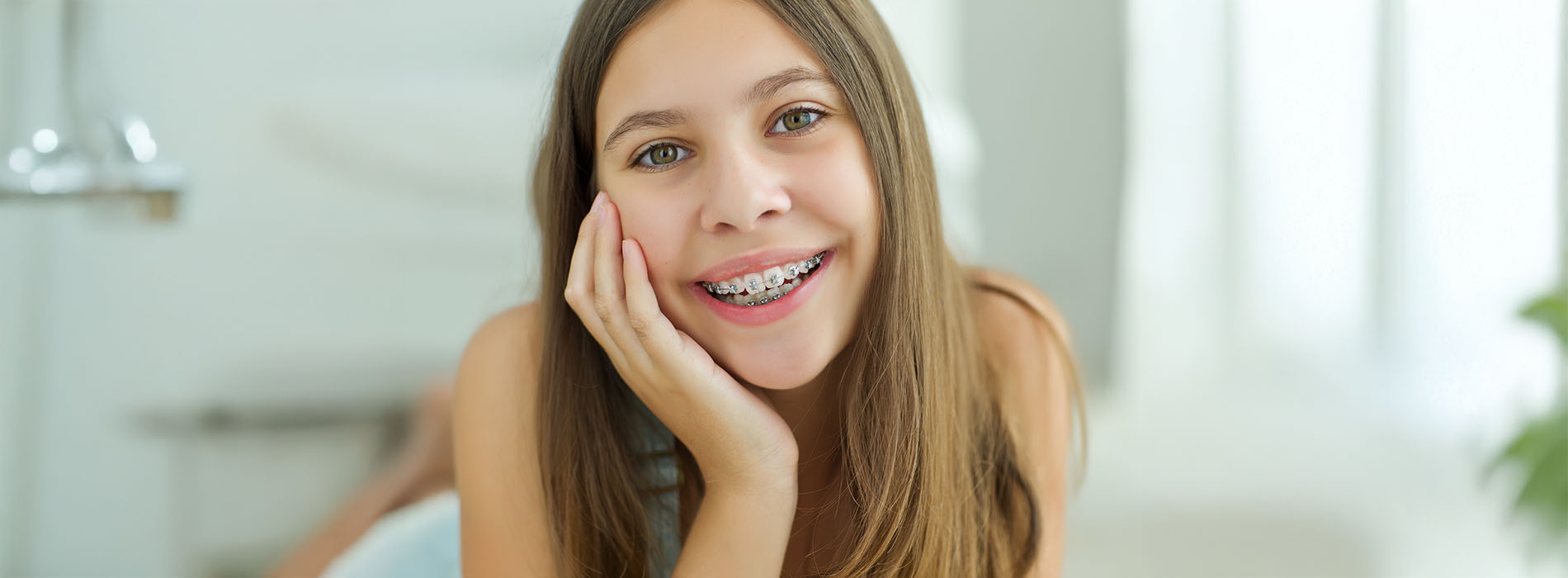 A young girl with a toothy smile poses for a picture in front of a bathroom mirror.