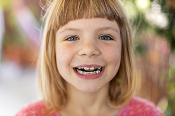 A young girl with a gap-toothed smile looks directly at the camera.