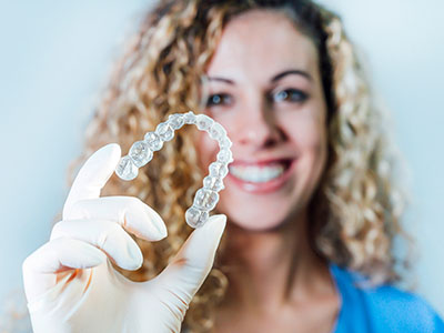 A person holding up a clear dental retainer with their hand.