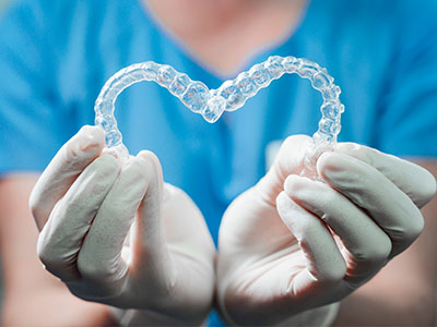 A hand holding a clear plastic heart shaped like a mouthguard with a blue background.