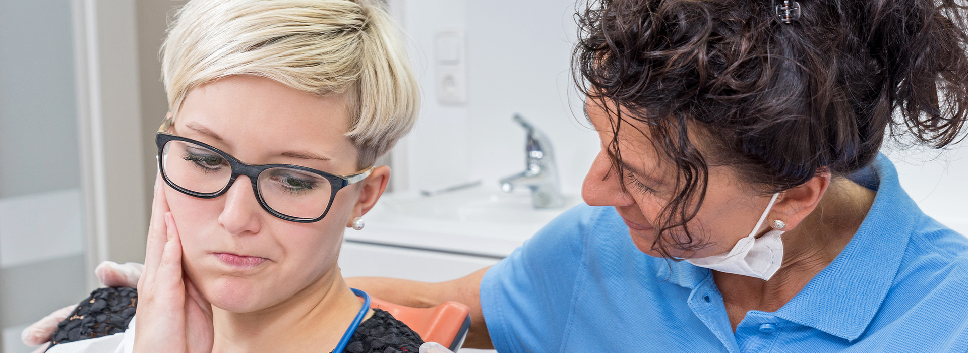 The image depicts two individuals in a dental office setting, with one person receiving dental care from another.